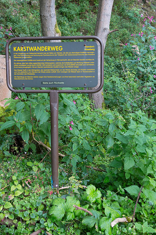 Schild mit Tücke: "Siehe auch Rückseite" durch die Brennesseln?