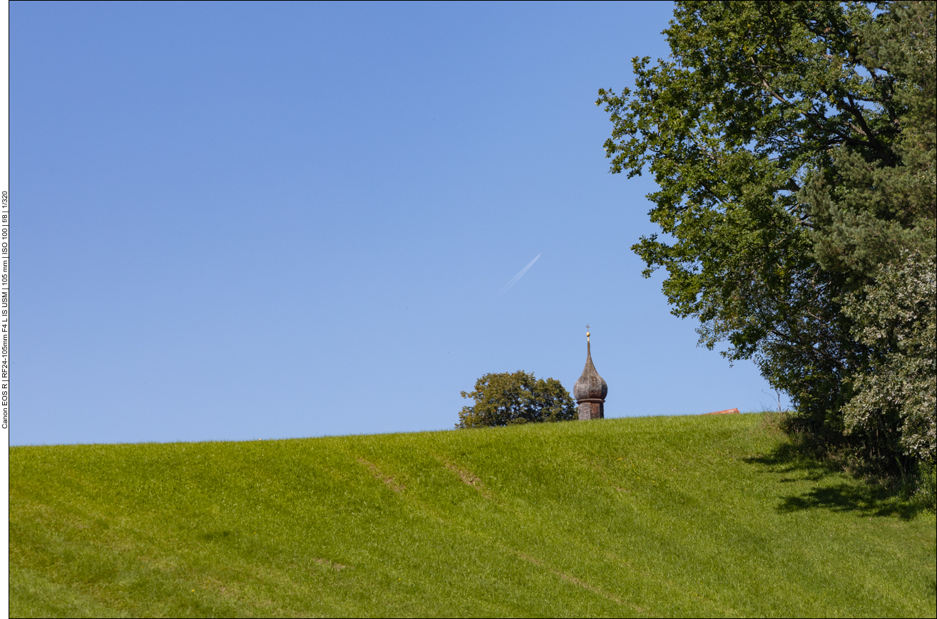 Kirchturm spitzt hinter dem Hügel hervor