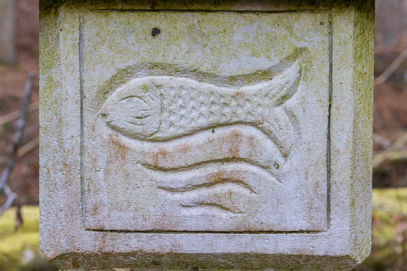 Fisch und Wellen als Steinbildhauerei unter dem Infoschild